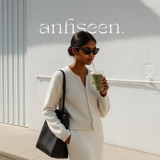 Stylish South Asian woman in a minimalist cream cardigan and skirt set, walking in sunlight with a green smoothie and black sunglasses, embodying clean girl aesthetic.