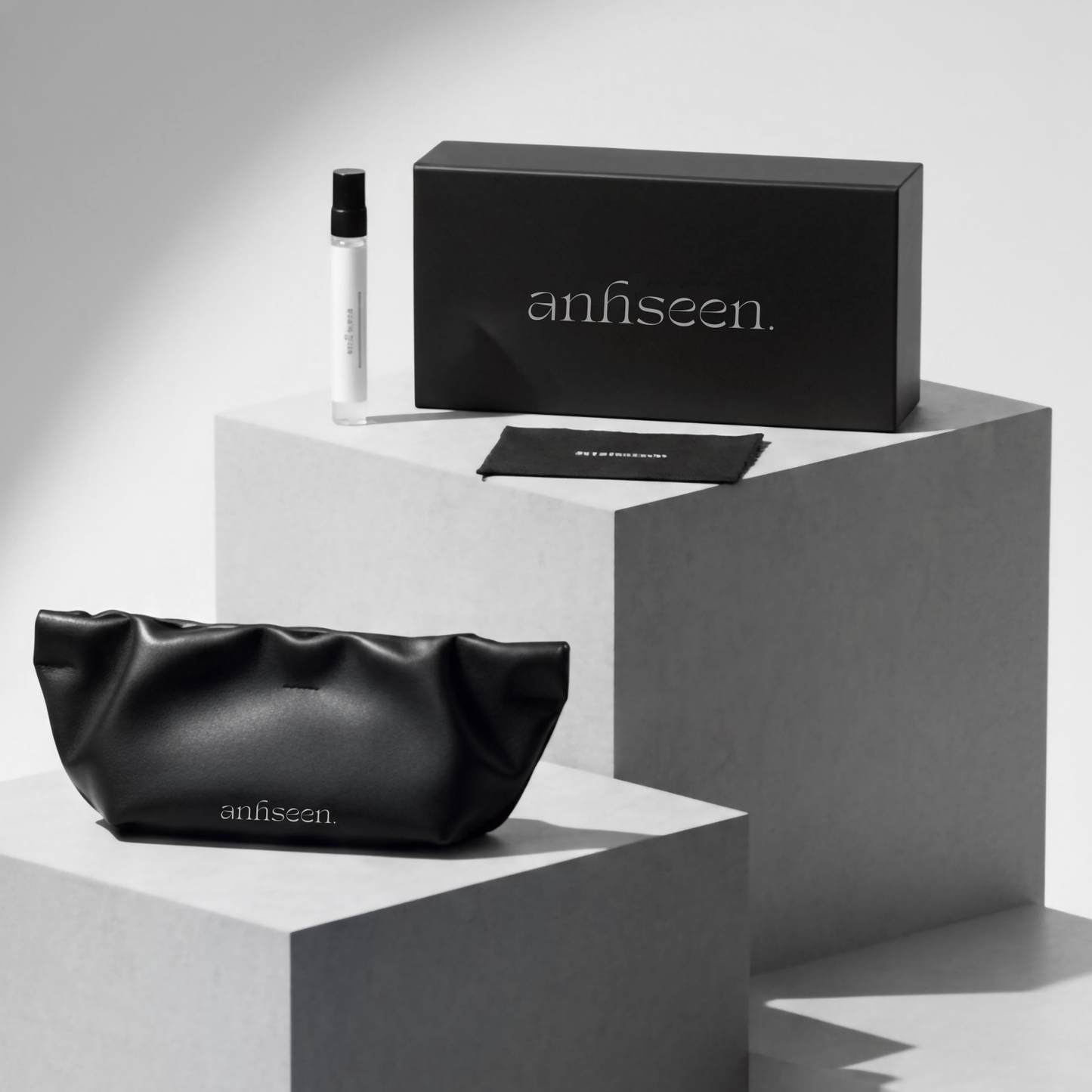 Premium Anhseen eyewear packaging displayed on minimalist grey plinths, featuring the black sunglasses box, branded leather pouch, microfiber cloth and lens care spray, showcasing luxury Asian-fit eyewear accessories.